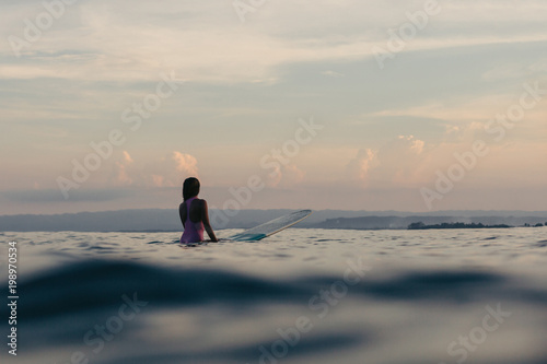 silhouette of surfer sitting on surfboard in water in sea at sunset