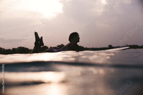 silhouette of sportswoman lying on surfing board in ocean on sunset © LIGHTFIELD STUDIOS