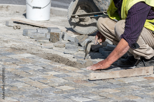 Construction worker installing stone blocks on the street.