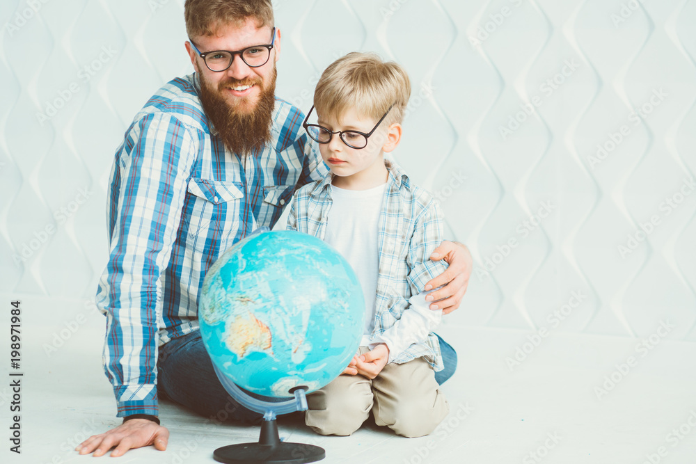 Beard hipster father and son in eyeglasses looking at globe over white polygonal wall background. Toned Beard hipster father and son in eyeglasses looking at globe over white polygonal wall background. Toned