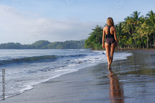 Back view of young girl walking on tropical beach near ocean
