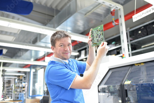 Arbeiter prüft Platine in der Fertigung für Elektronik einer Fabrik // Worker tests motherboard in the production of electronics for a factory