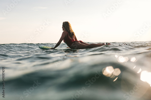 woman in swimming suit lying on surfing board in ocean