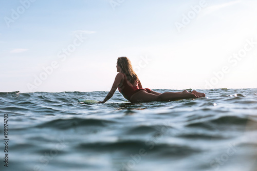 woman in swimming suit lying on surfing board in ocean on sunny day