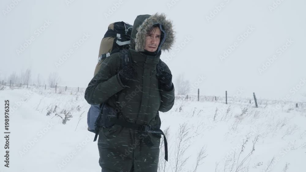 Young man with backpack walking through a snowstorm in the snowy wilderness, struggling wind and extreme cold.