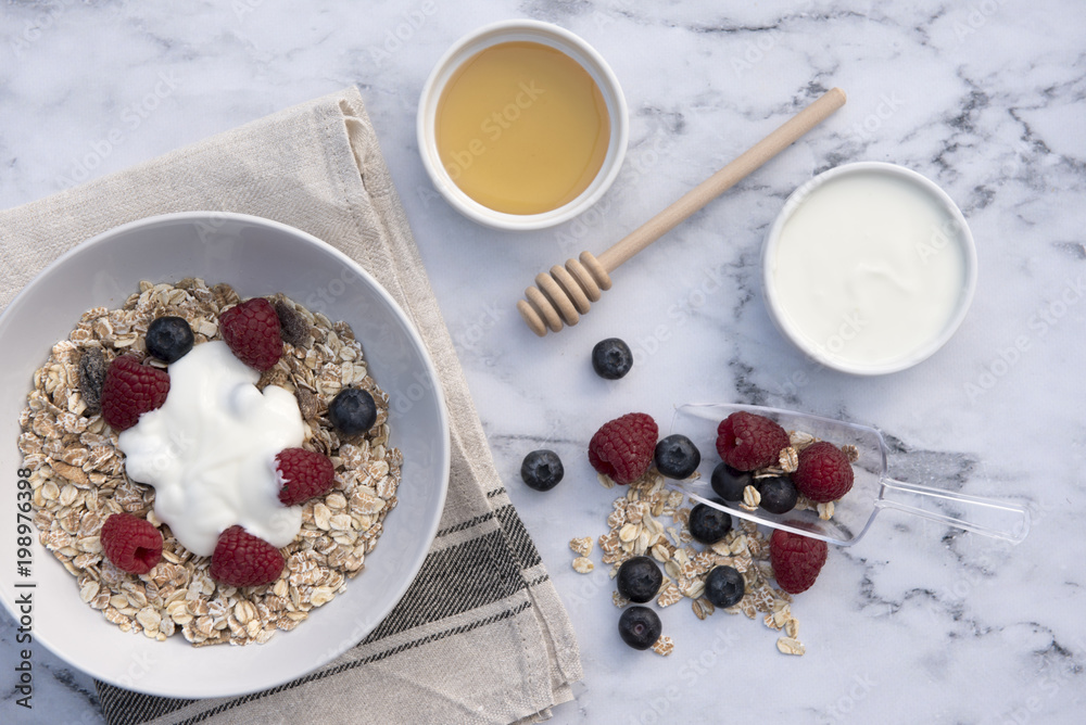 White bowl of muesli with raspberries, blueberries and a pot of honey and yogurt White bowl of muesli with raspberries, blueberries and a pot of honey and yogurt