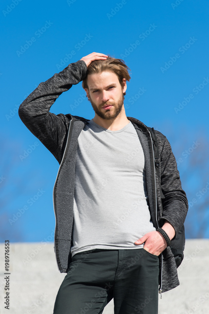 Fototapeta premium Mens fashion and style. Man with beard in casual wear touch hair on sunny outdoor, fashion. Macho stand on blue sky, perspective. Perspective, future, freedom.