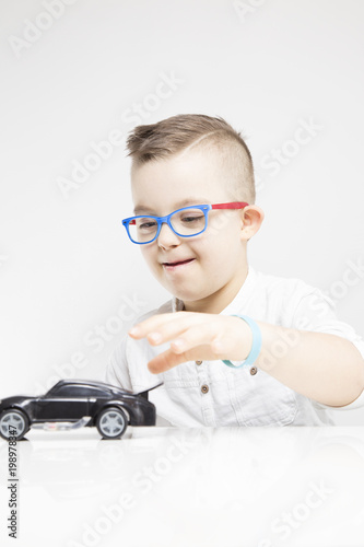 Uśmiechnięty chłopiec z zespołem Downa bawi się samochodem. 