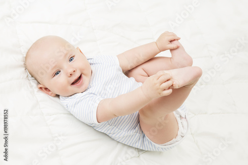 Φωτογραφία Baby Lying on Back, Happy Smiling Kid Holding Legs in Hands, Newborn Child Lie o