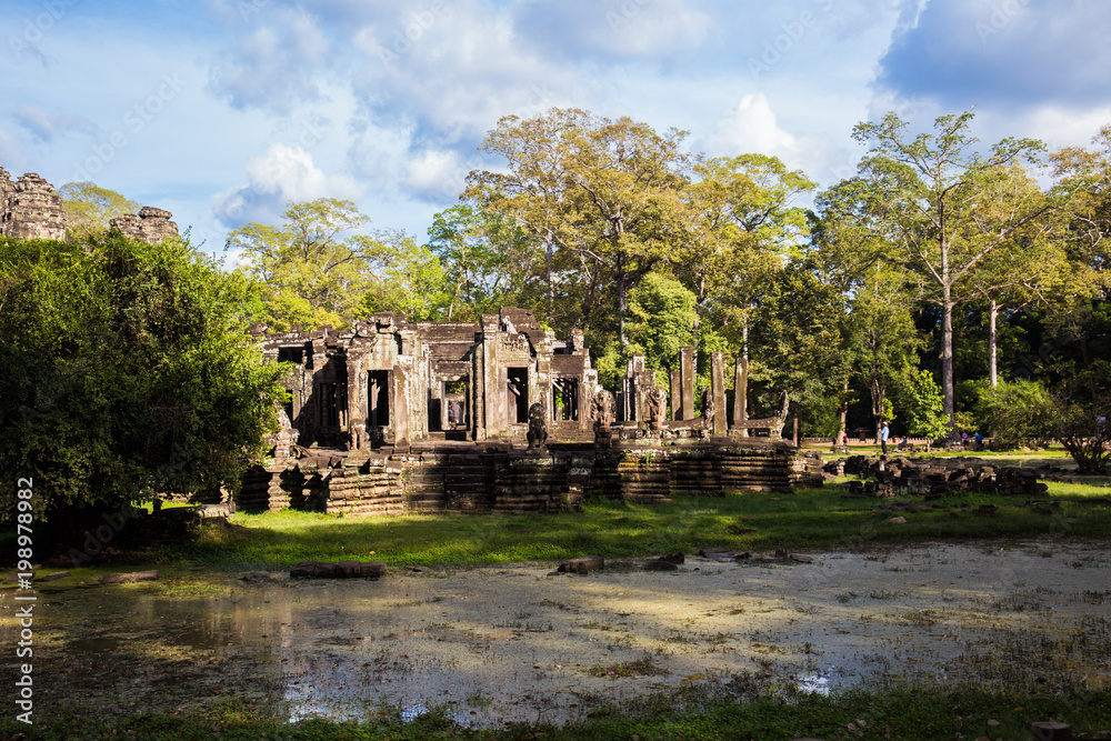 ancient public temple with tourist walk around and small lake infront with blue sky in cambodia