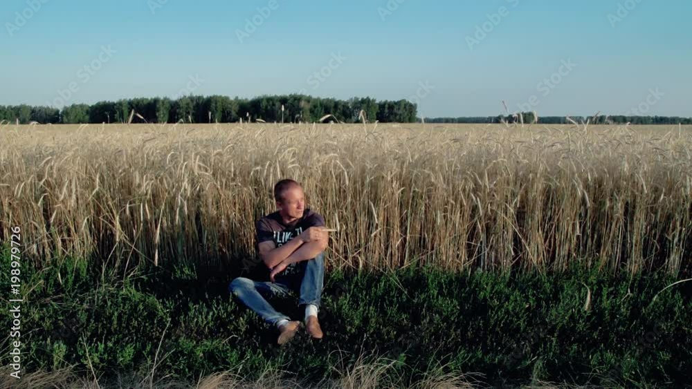 Young man sitting near the field of rye, dreamily looking at the sky, in his head the music, he hops foot to the beat Young man sitting near the field of rye, dreamily looking at the sky, in his head the music, he hops foot to the beat