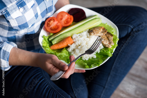 Girl with a plate of vegetables in hands. Healthy eating concept. A girl in jeans and a plaid shirt. Casual Style. Proper nutrition. Diet. Health. Chicken meat with spices. Small depth of field. photo