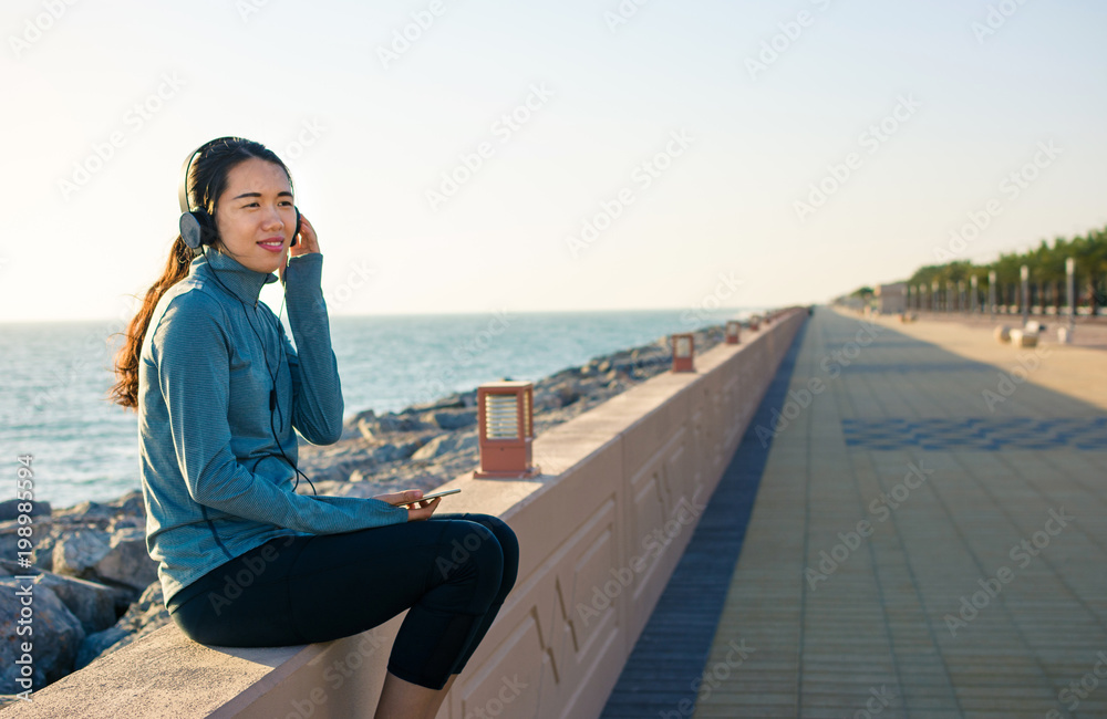Girl listening to music by the seaside and enjoying sunny day