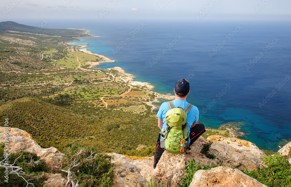 man with backpack sitting on a rock and looking at the Mediterranean Sea