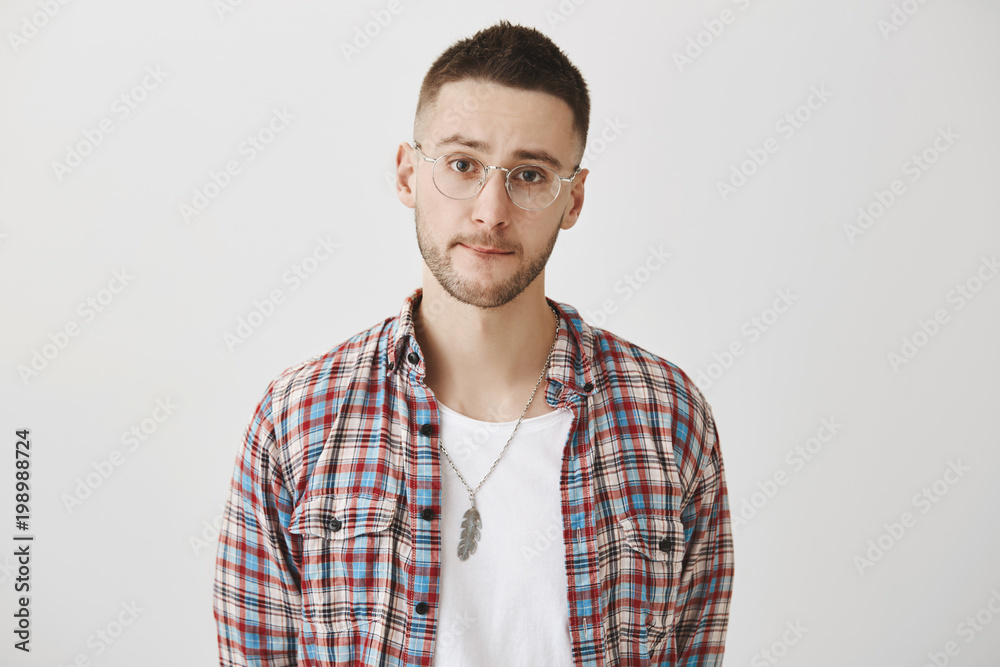 Portrait of sad gloomy guy with glasses, wearing plaid shirt over white t-shirt, sucking lips and frowning, hesitating over gray background. Man wants to say truth but knows it will upset girlfriend Portrait of sad gloomy guy with glasses, wearing plaid shirt over white t-shirt, sucking lips and frowning, hesitating over gray background. Man wants to say truth but knows it will upset girlfriend