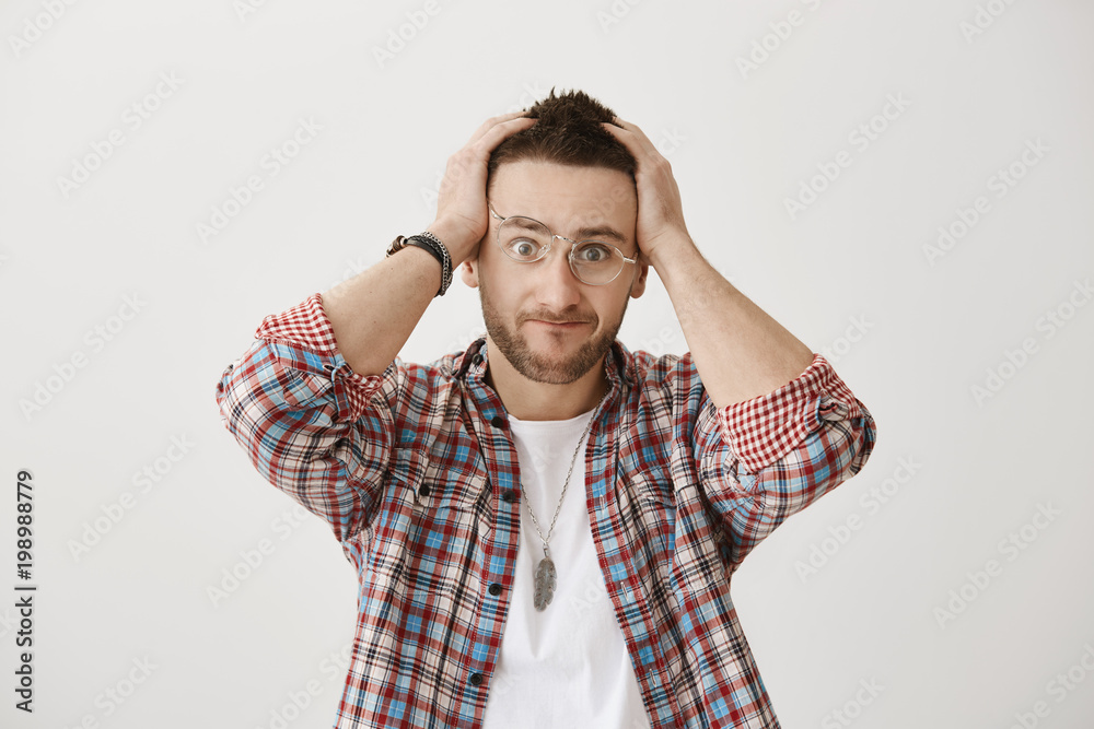 My brain aches from your scream. Studio shot of bothered and annoyed attractive caucasian male with beard, wearing stylish glasses and holding hands on head, being distracted under pressure. My brain aches from your scream. Studio shot of bothered and annoyed attractive caucasian male with beard, wearing stylish glasses and holding hands on head, being distracted under pressure.