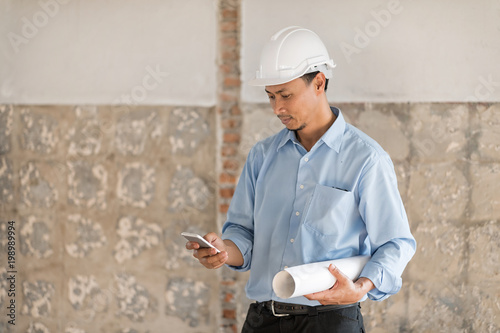 Young Asian engineer or technician man smiling with safety helmat and holding plans. photo