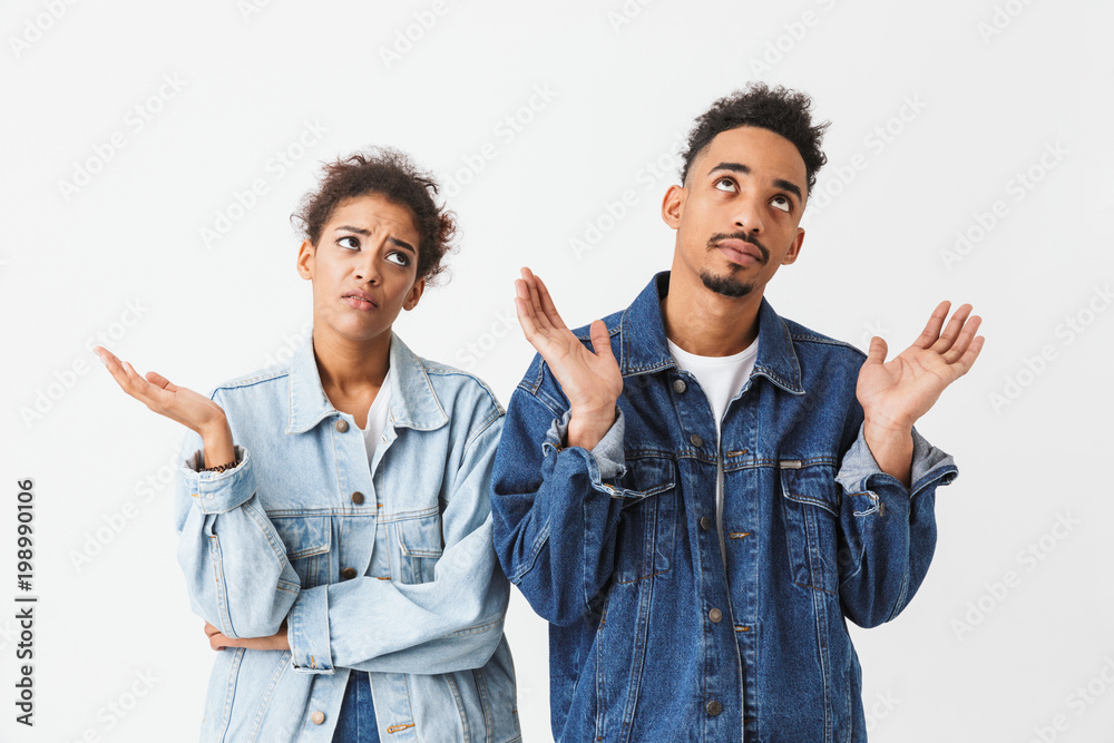 Confused couple in denim shirts standing together and looking up Confused couple in denim shirts standing together and looking up