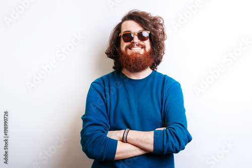 Portrait of cheerful bearded hipster man with long curly hair and wearing sunglasses with crossed arms © Vulp