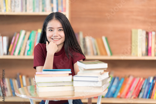Cheerful girl sitting by wooden table and Reading book in library.Smiling to camera.