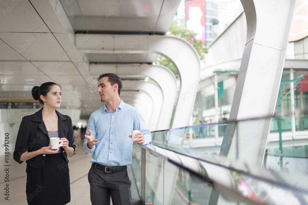 Two colleagues walking in street of city talking to each other while holding disposable coffee cups. Two colleagues walking in street of city talking to each other while holding disposable coffee cups.