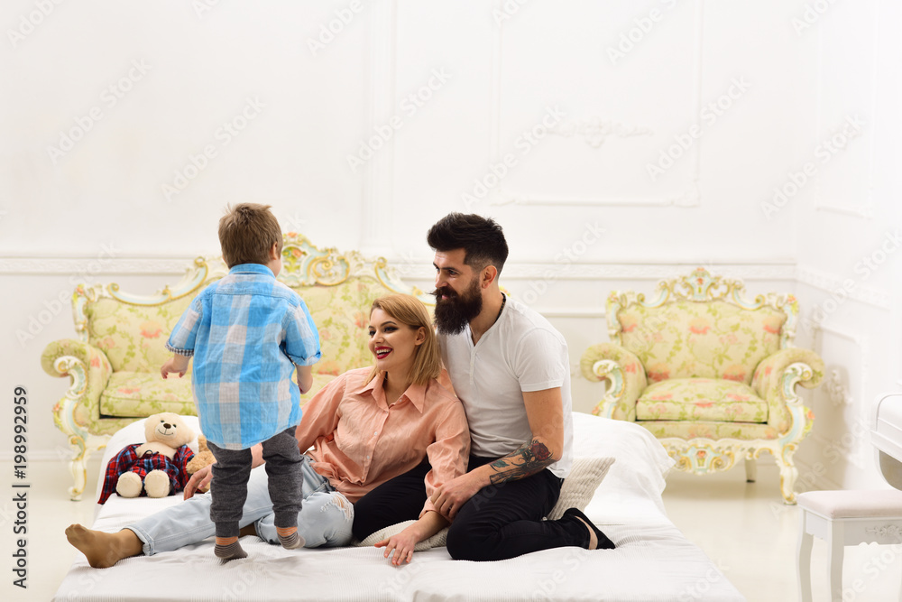 Young family spend time together in bedroom on bed, luxury interior background. Mother and father cuddling while listening their cute little son. Parents pay attention to kid. Happy family concept. Young family spend time together in bedroom on bed, luxury interior background. Mother and father cuddling while listening their cute little son. Parents pay attention to kid. Happy family concept.
