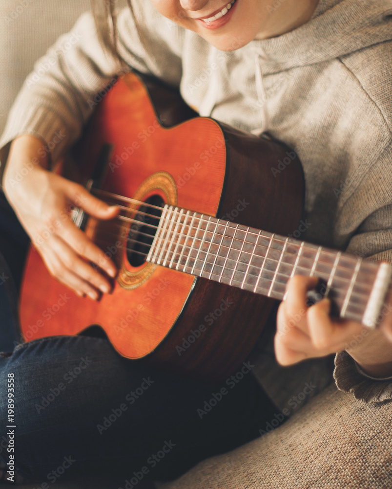 Young woman musician guitarist playing guitar at home