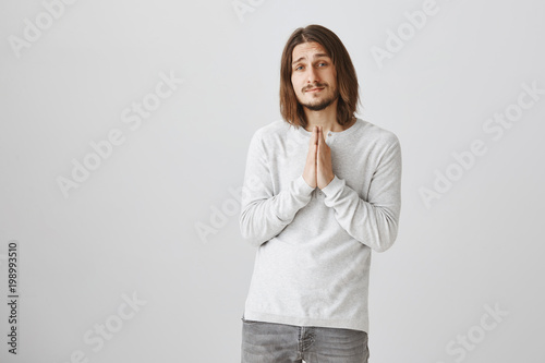 How you can reject this cute eyes. Portrait of handsome young male teacher holding hands in pray, begging coworker to cover him at work, asking for favour with angel expression over gray background