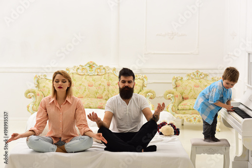 Obraz na plátně Young parents meditating, while their little son playing piano, annoying mother and father