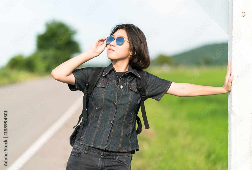 Woman stand with backpack hitchhiking along a road