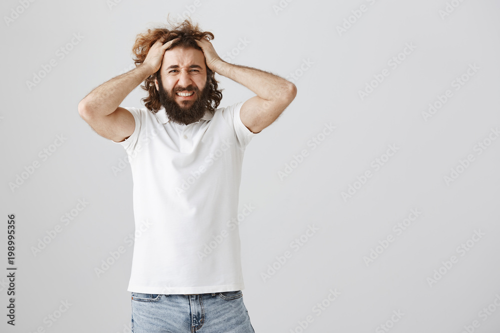 Guy loses temper from bad luck. Portrait of miserable and depressed young eastern man with beard pulling hair with both hands and grimacing from painful emotions, feeling regret that he lost Guy loses temper from bad luck. Portrait of miserable and depressed young eastern man with beard pulling hair with both hands and grimacing from painful emotions, feeling regret that he lost