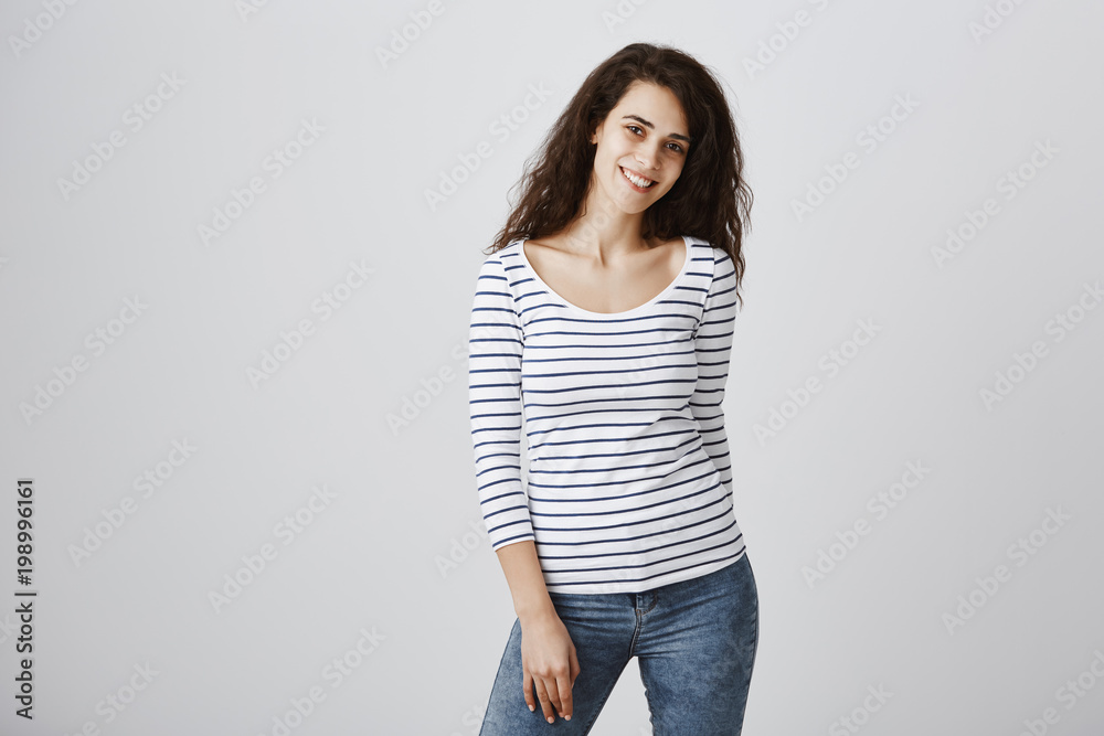 Attractive young girl with lot of dreams and life goals. Studio shot of beautiful curly-haired european female student in striped blouse posing and smiling cheerfully, expressing friendly attitude