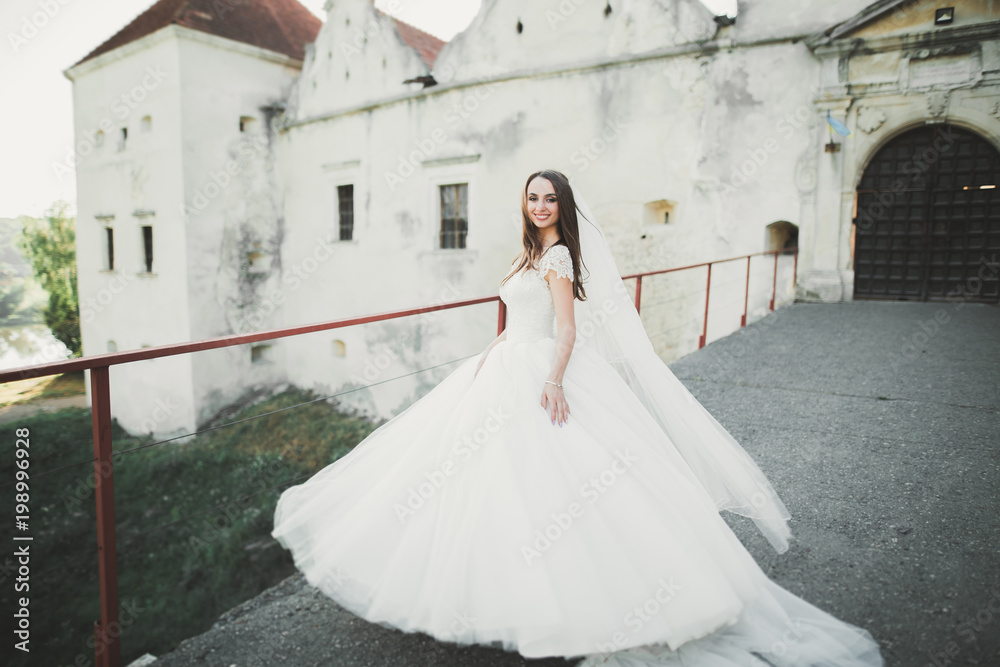 Fototapeta premium Beautiful brunette bride in elegant white dress holding bouquet posing neat trees