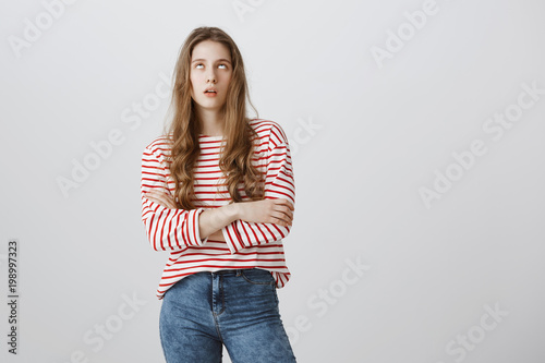 Teenagers hate when parents scolding. Bothered and annoyed european female student rolling eyes and sighing, standing with crossed arms over gray background, being bored and fed up of nonsense talks