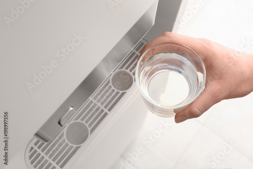 Woman with glass near water cooler, closeup