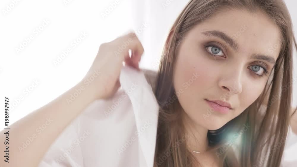 Young beautiful sexy caucasian girl putting on a white shirt, looking at the camera, touching the hair, portrait, temptation, white sunlight in the background 60 fps Young beautiful sexy caucasian girl putting on a white shirt, looking at the camera, touching the hair, portrait, temptation, white sunlight in the background 60 fps