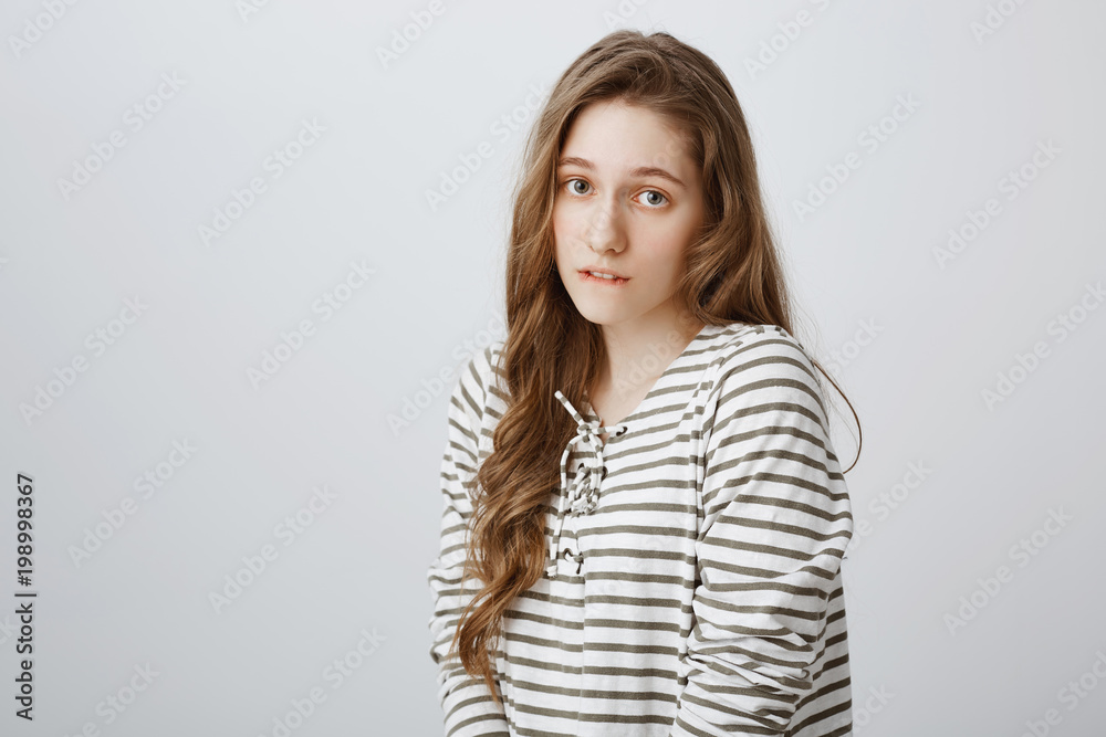 Girl glancing with angel expression. trying to persuade boyfriend she is innocent. Portrait of cute young woman standing over gray background, biting lip and being gloomy, begging or asking favour Girl glancing with angel expression. trying to persuade boyfriend she is innocent. Portrait of cute young woman standing over gray background, biting lip and being gloomy, begging or asking favour