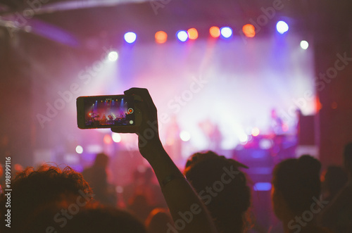 Recording a live show. Fan with hand up takes smartphone video at concert