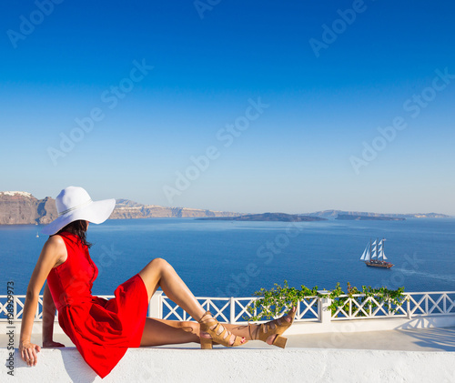 Santorini travel tourist brunette woman in red dress visiting famous white Oia village. photo