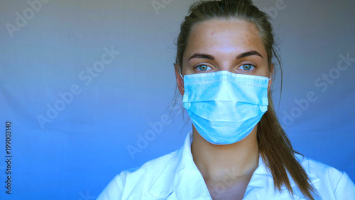 Young beautiful woman, nurse, doctor, in mask, white blue background.