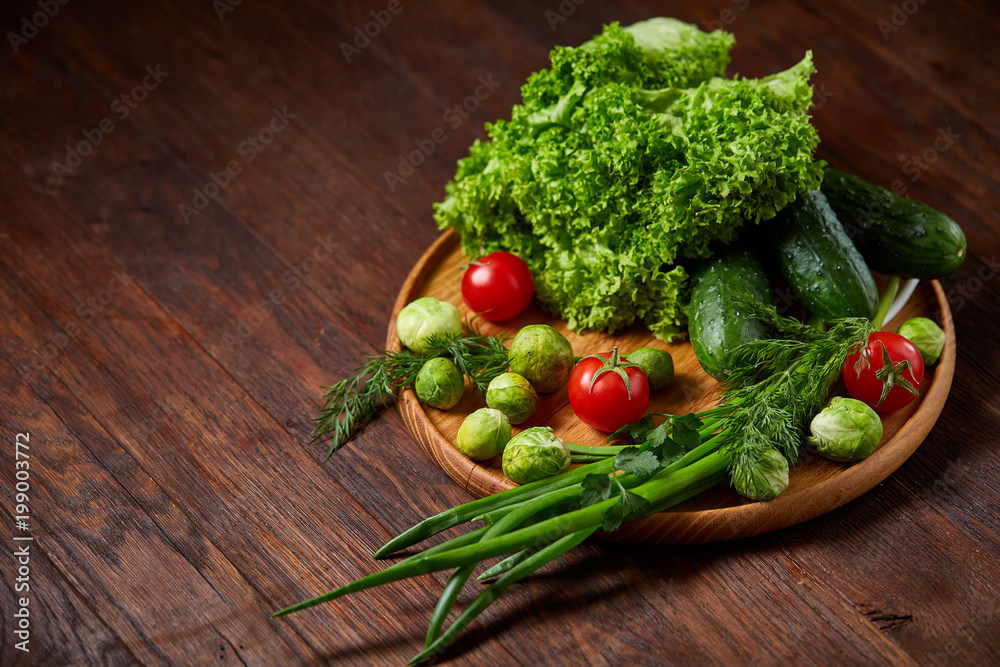 Vegetarian still life of fresh vegetables on wooden plate over rustic background, close-up, flat lay.