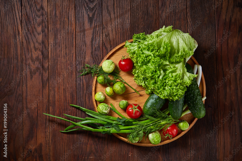 Vegetarian still life of fresh vegetables on wooden plate over rustic background, close-up, flat lay. Vegetarian still life of fresh vegetables on wooden plate over rustic background, close-up, flat lay.