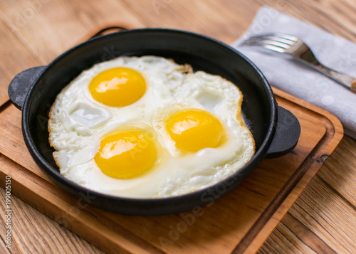 Fried eggs in a frying pan on a wooden background.