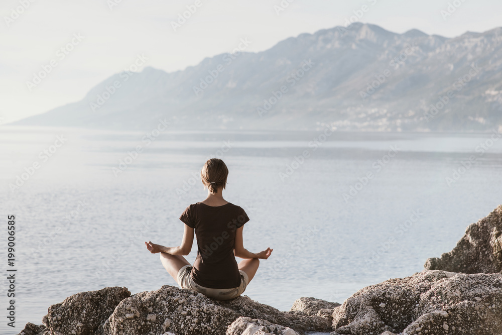 Fototapeta premium Young woman practicing yoga near the sea. Harmony and meditation concept. Healthy lifestyle