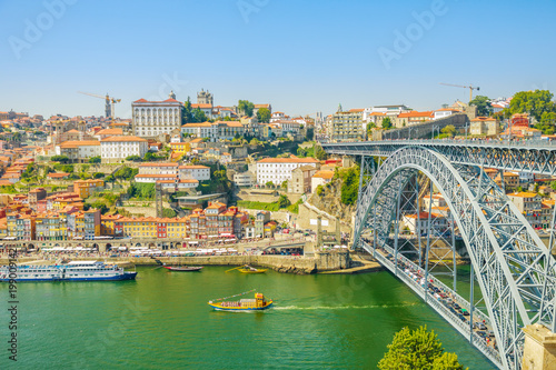 Tourist boats cruising under Douro River in Porto. Aerial view of Dom Luis I Bridge, Ribeira Waterfront and Rabelo boats from Vila Nova de Gaia, Porto, Portugal. Oporto urban cityscape in blue sky.