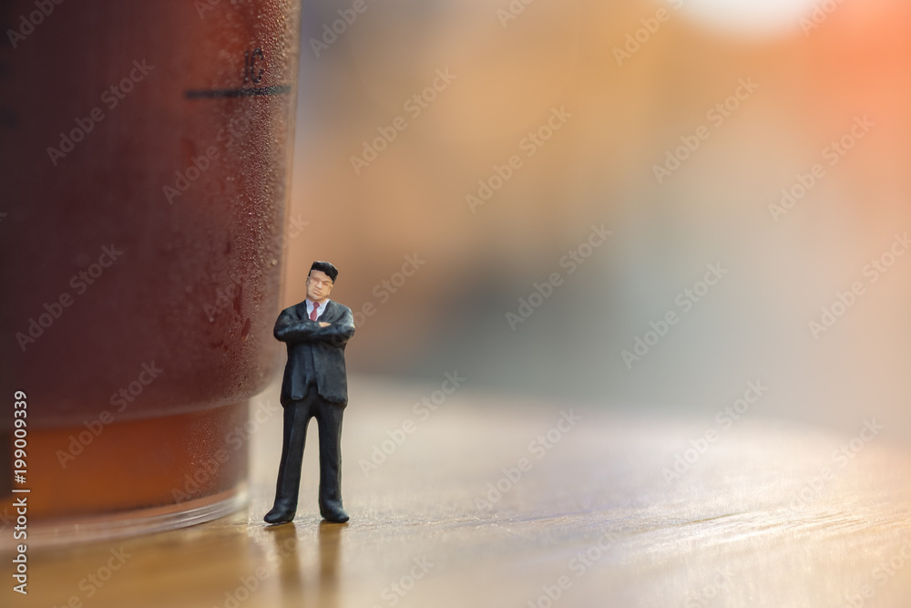 Business planning concept. Businessman miniature figure standing and thinking with plastic cup of iced black coffee (Americano) Business planning concept. Businessman miniature figure standing and thinking with plastic cup of iced black coffee (Americano)