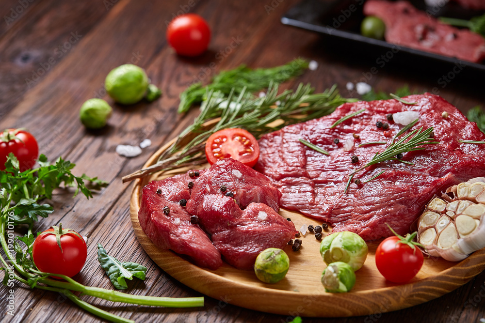 Still life of raw beef meat with vegetables on wooden plate over vintage background, top view, selective focus