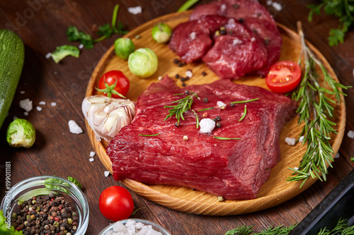 Still life of raw beef meat with vegetables on wooden plate over vintage background, top view, selective focus