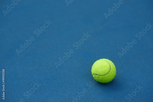 Yellow bright tennis ball is lying on on blue carpet. Made for playing tennis. Contrast image with satureted colors. Blue tennis court.