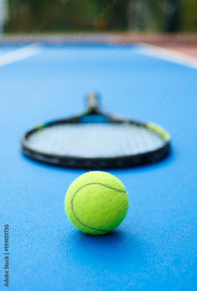 Yellow ball is laying on professional tennis racket background. A ball is on blue bright tennis cort carpet. Photo made in contrast saturated colors. Concept of sport equipment photo.